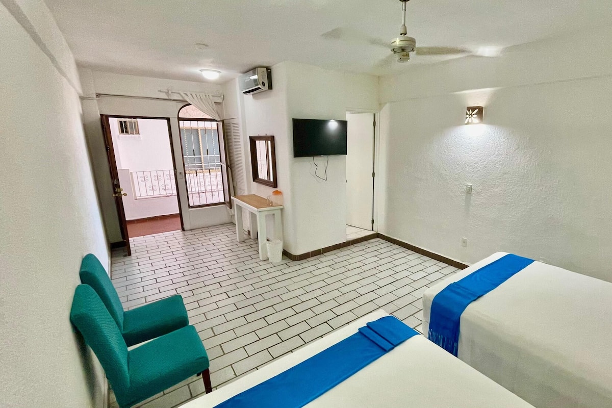 Una habitación de hotel con cama, escritorio, silla, televisión y balcón.
