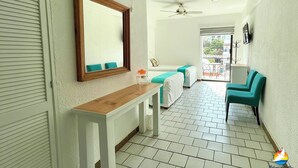 A hotel room with a large mirror, a ceiling fan, a wooden console table, a bed with a green bedspread, a small table with a lamp, and a view of the outside balcony. - Paloma Del Mar  (Puerto Vallarta)