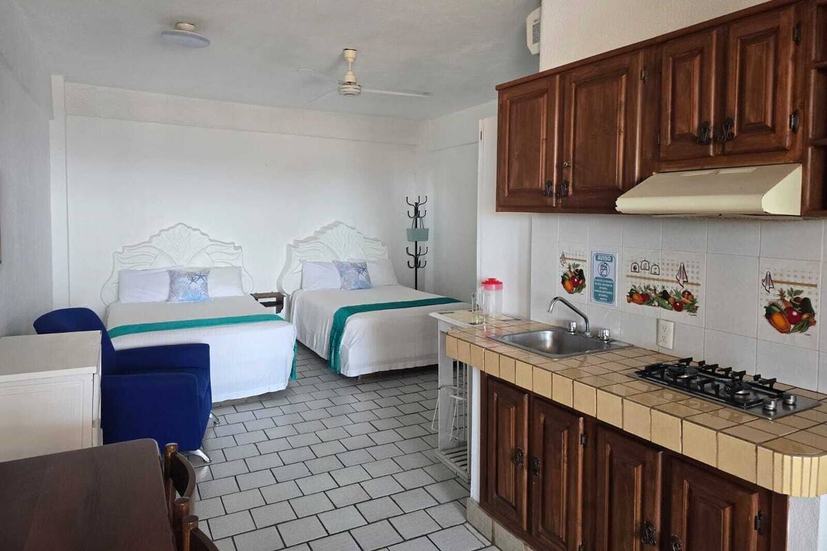 Una habitación de hotel compacta con dos camas, una kitchenette pequeña y un baño.