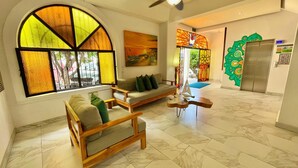 A spacious living area with a large arched window, a sofa, a wooden chair, and a small table with a decorative item. - Paloma Del Mar  (Puerto Vallarta)