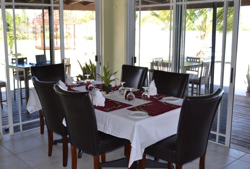 A dining area with a table set for four, surrounded by chairs, and large windows offering a view of the outdoors.