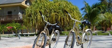 Una bicicleta estacionada frente a un edificio con balcón, rodeada de palmeras y un cielo despejado.