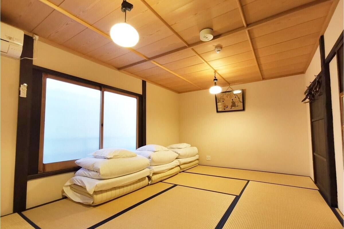A traditional Japanese room with tatami flooring, a futon bed, and a large window.