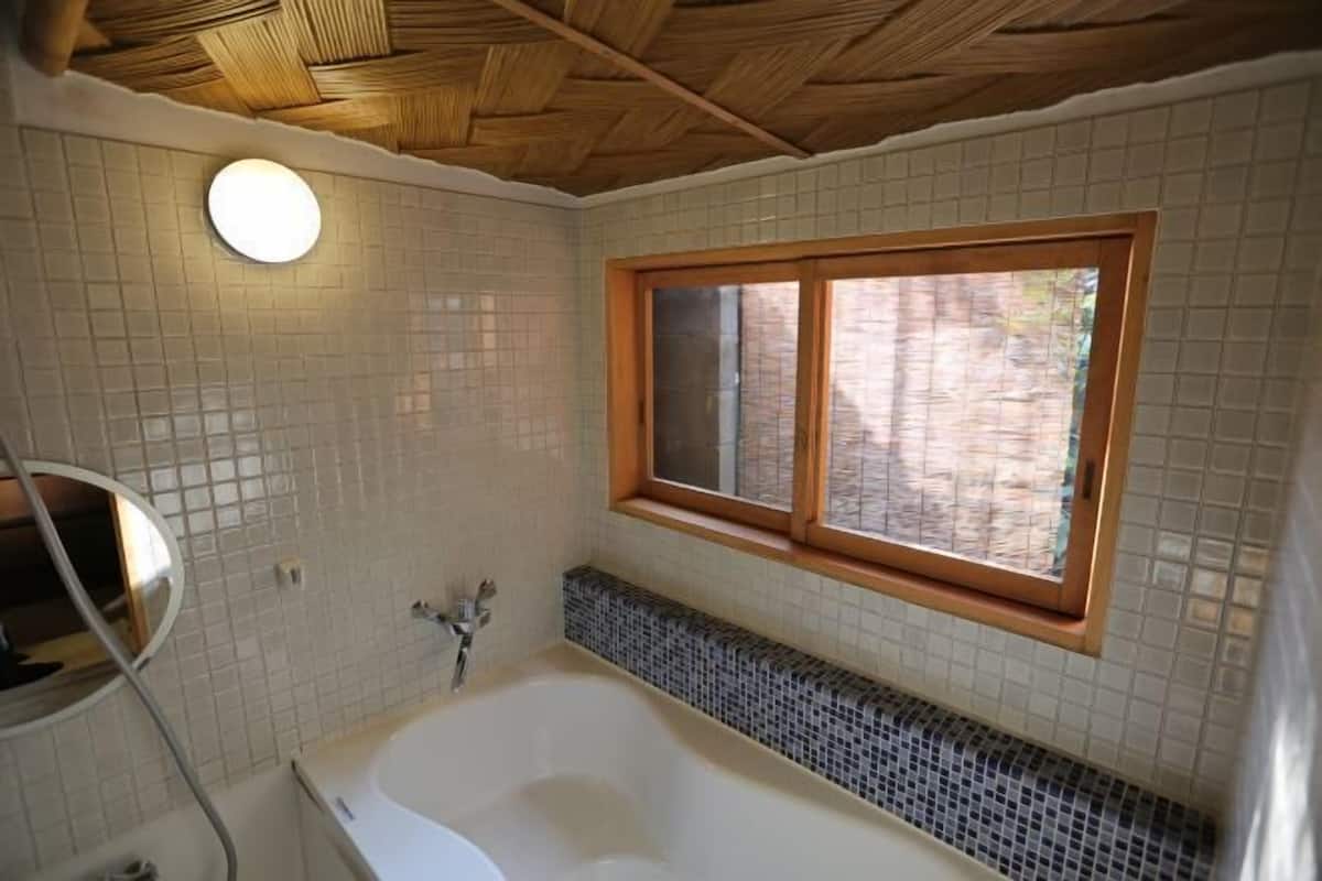 A bathroom with a bathtub, a window, and a tiled wall.