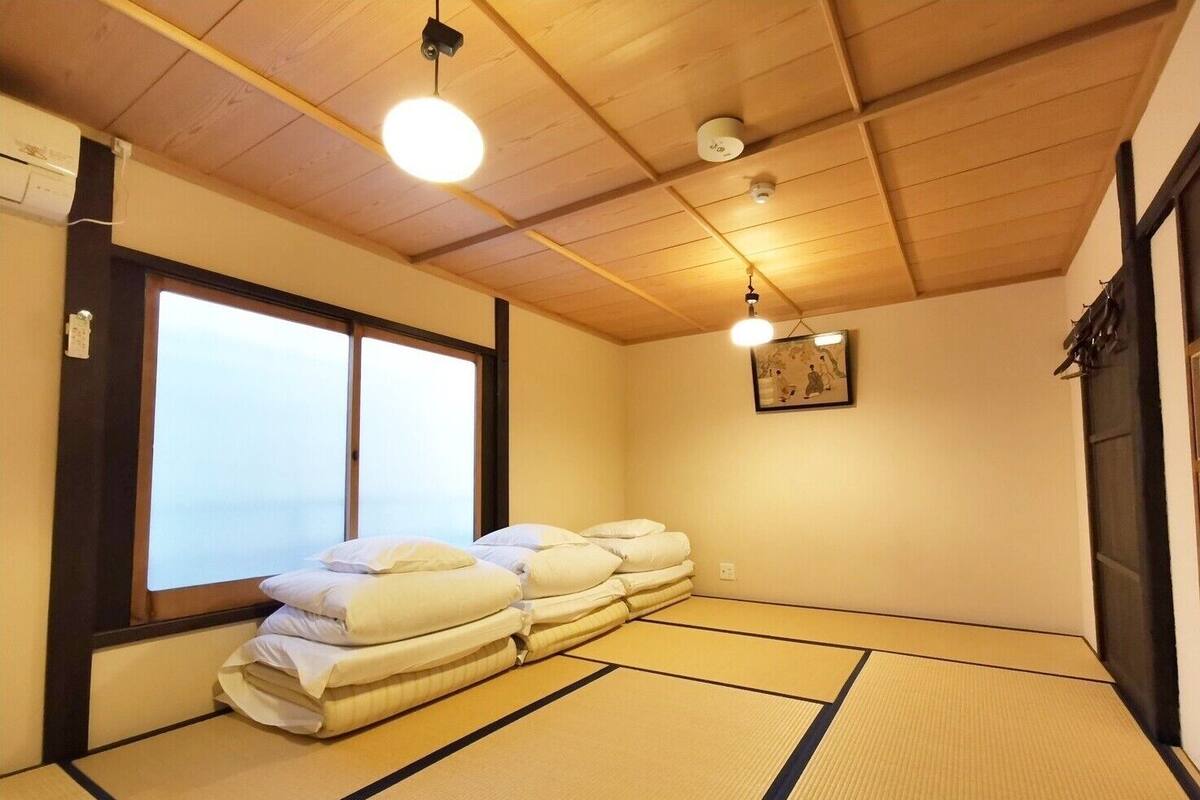 A traditional Japanese room with tatami flooring, a futon bed, and a large window.