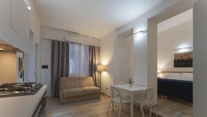 A compact living space with a kitchenette, a sofa, a dining table with chairs, and a bed. - Dalmati House (Rome)