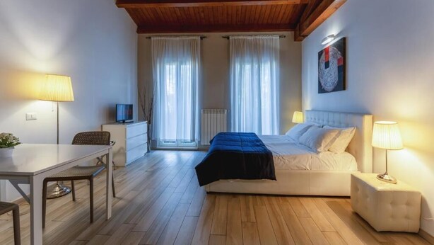 A bedroom with a bed, bedside table, lamp, and a TV on a small table. - Dalmati House (Rome)