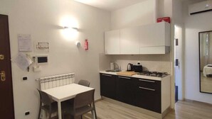A modern kitchen with white cabinets, a dining table with chairs, and a built-in stove. - Dalmati House (Rome)