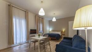 A hotel room with a bed, a sofa, a desk with a chair, a TV, and a lamp. - Dalmati House (Rome)