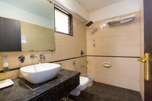 A bathroom with a white sink, a mirror, a shower, and a toilet. - Sukh Hotel (Mumbai)