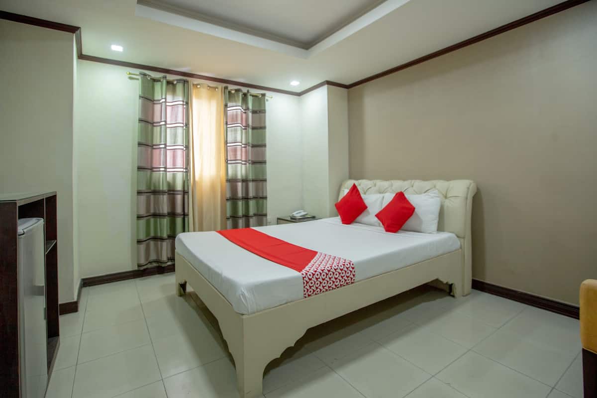 A hotel room with a bed, curtains, a nightstand, and a chair.