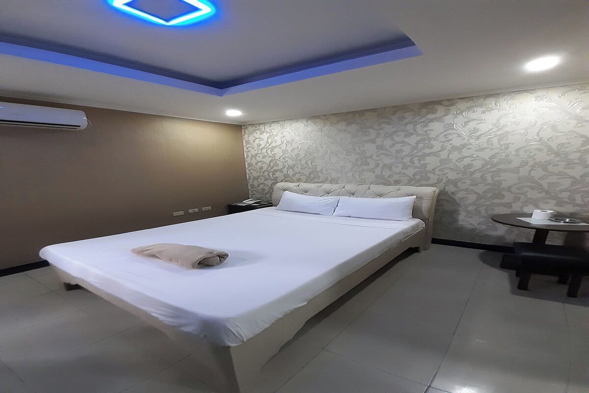 A hotel room with a bed, bedside table, and a small round table with a chair.
