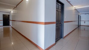 A long, narrow hallway with white walls and wooden trim, leading to a door. - OYO 700 Pj Inn Hotel (Angeles City)