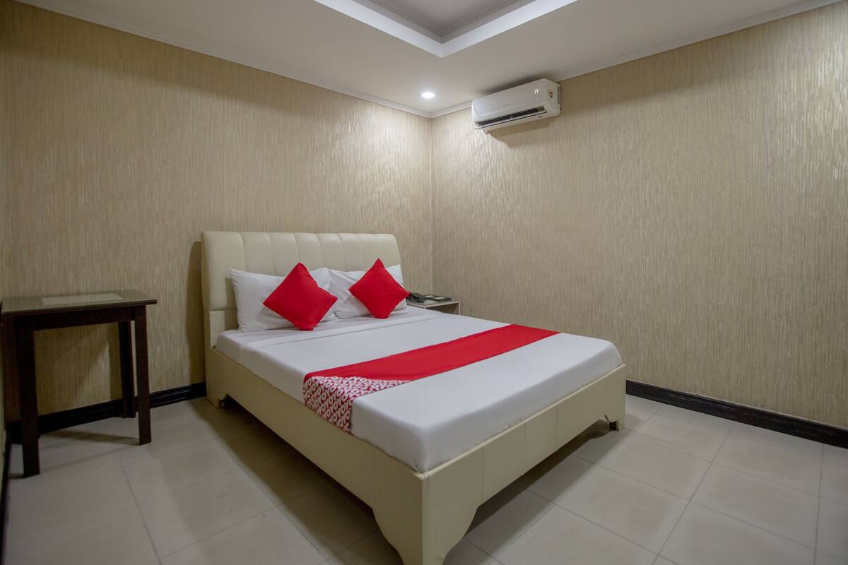 A hotel room with a bed, a bedside table, and an air conditioning unit.