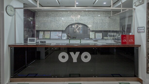 A reception desk with a glass front, a clock on the wall, and a sign indicating check-in and check-out times. - OYO 700 Pj Inn Hotel (Angeles City)