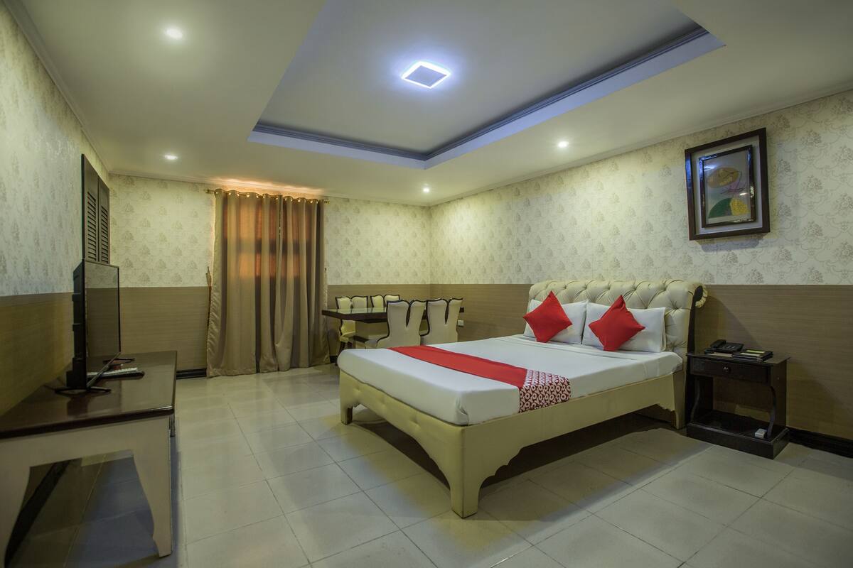 A hotel room with a large bed, bedside tables, a desk, a chair, and a TV.