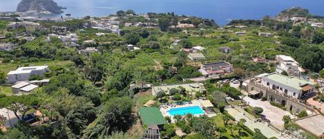 Vista aérea de una zona residencial costera con piscina, abundante vegetación y casas de arquitectura mediterránea.