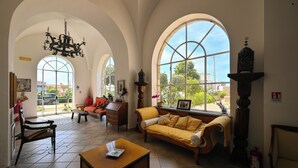 A spacious living room with high arched windows, a chandelier, and a sofa with a yellow throw. - Villa Tara (Serrara Fontana)