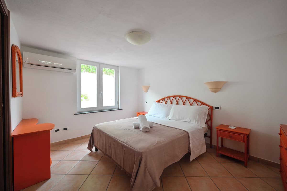 A bedroom with a bed, a nightstand, a dresser, an air conditioning unit, and a window.