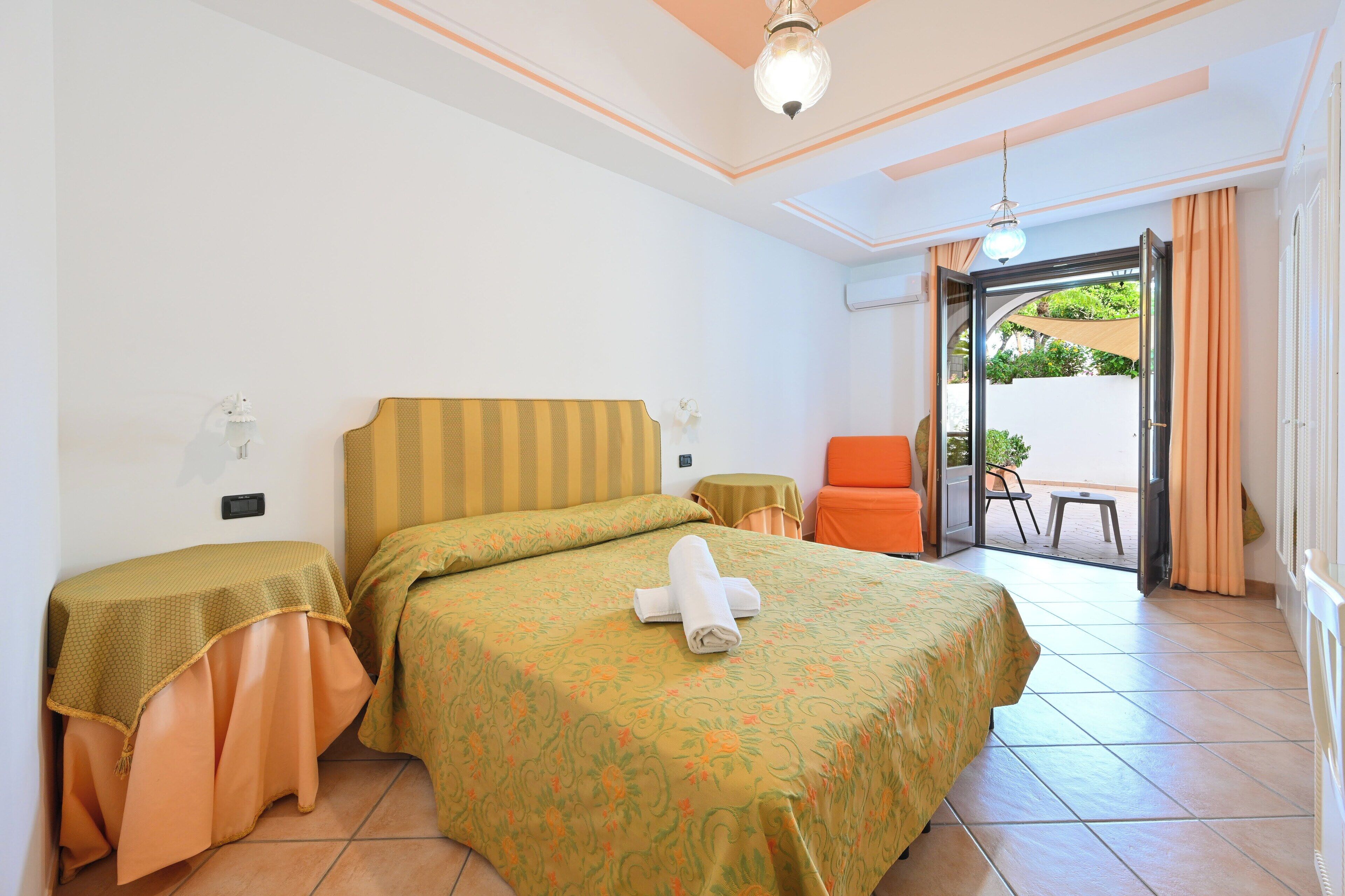 Un cuarto de hotel con una cama, dos mesitas de noche, una silla y vistas al exterior.