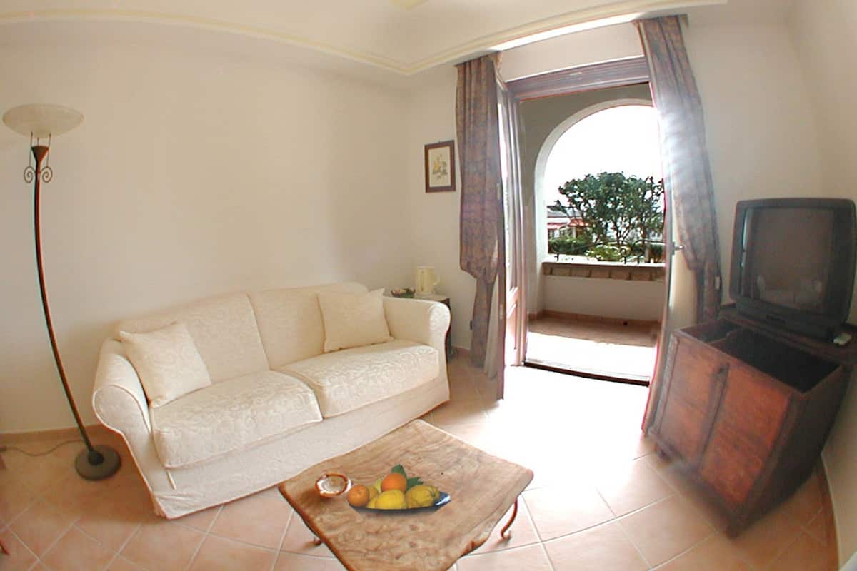 A living room with a sofa, a coffee table with fruits, a TV stand, and a floor lamp.
