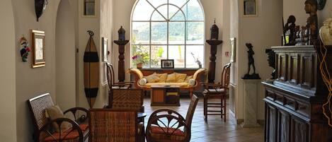 Uma sala de estar ampla com uma grande janela em arco, um sofá e diversas poltronas.