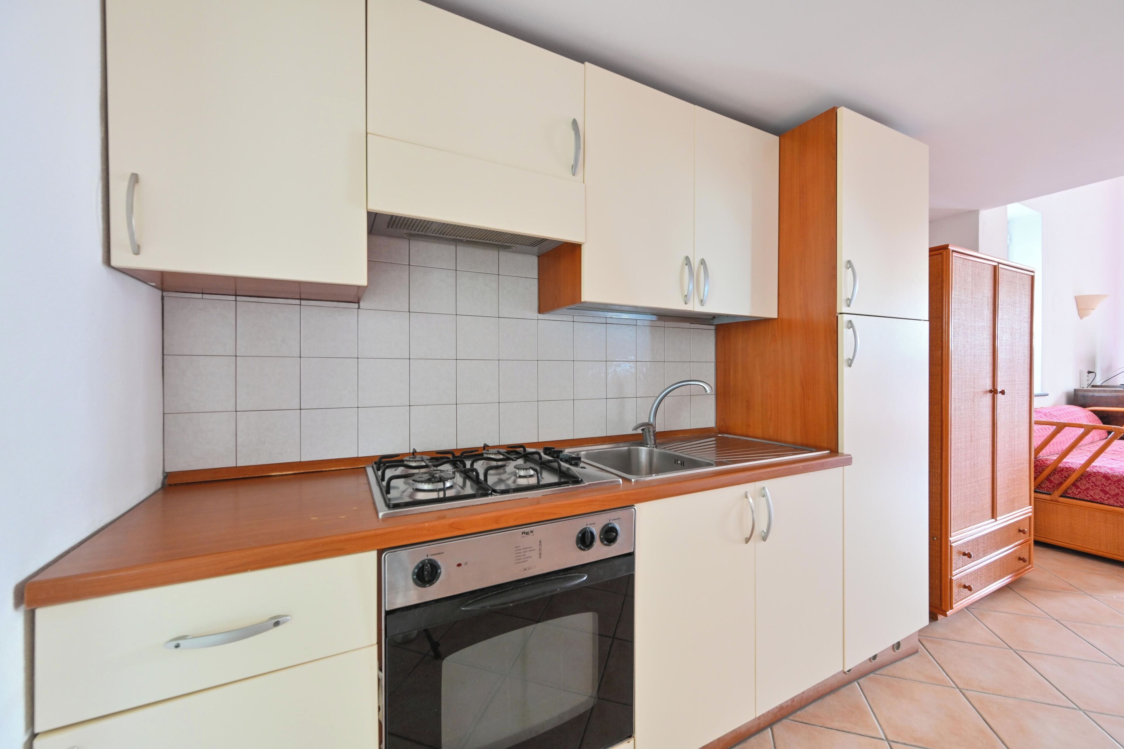A compact kitchen with white cabinets, a gas stove, a sink, and a small oven.