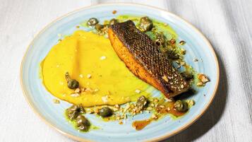 A plate with a piece of salmon, capers, and a yellow sauce.
