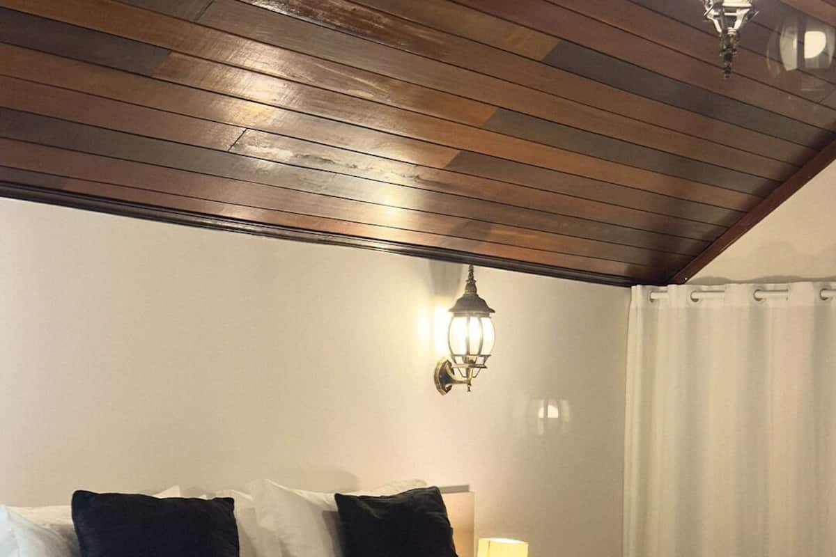 Una habitación de hotel con una cama grande, una mesita de noche con lámpara y techo de madera.