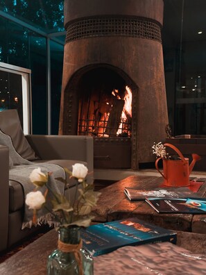 Een gezellige woonkamer met een stenen openhaard, een comfortabele bank, een houten salontafel met boeken en een bloevas.