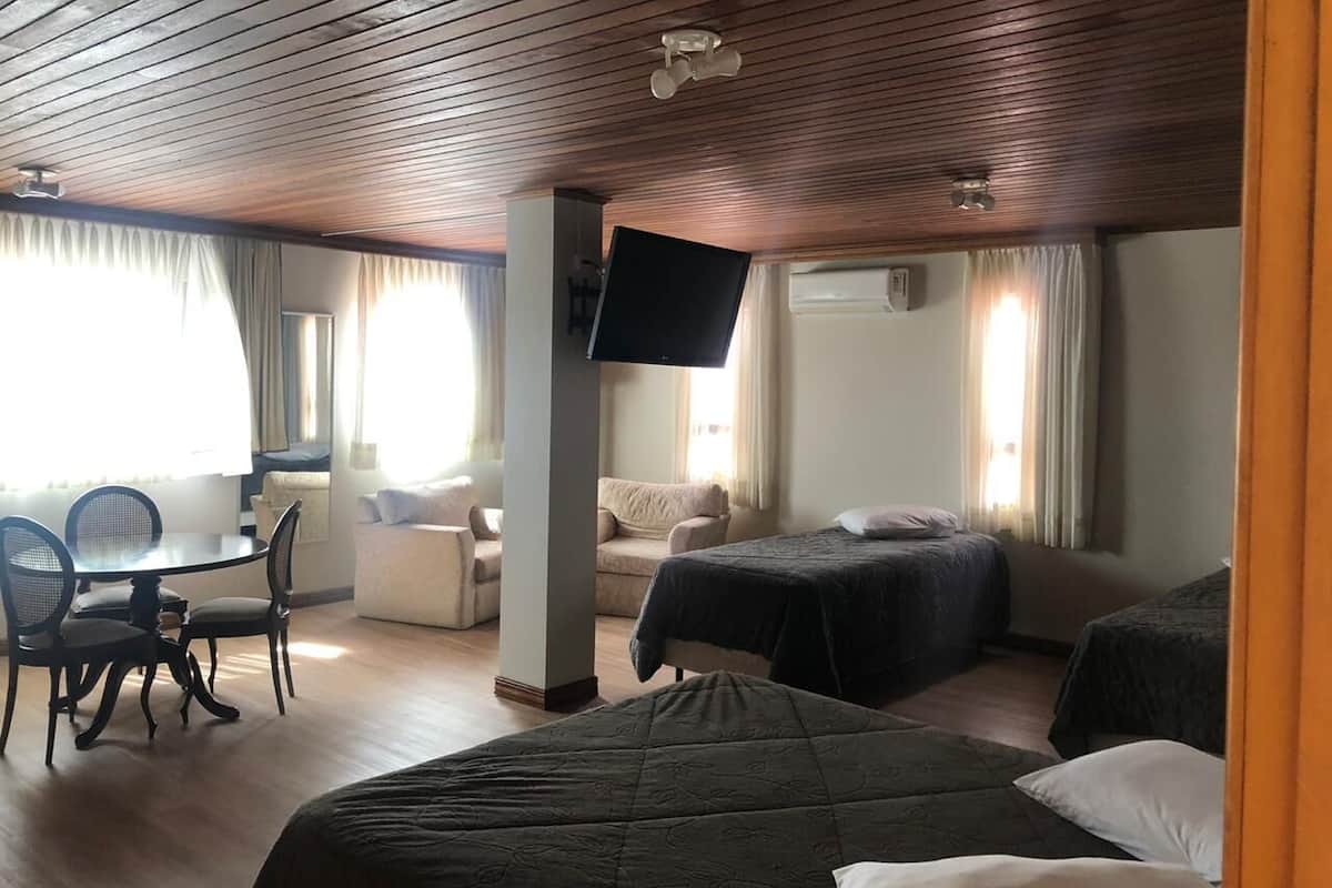 Habitación de hotel con techo de madera, un televisor de pantalla plana en la pared, una mesa de comedor con sillas, un sofá y dos camas individuales.