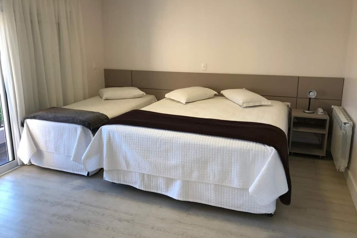 Una cama doble con cabecera, una mesita de noche con lámpara y una ventana con cortinas.