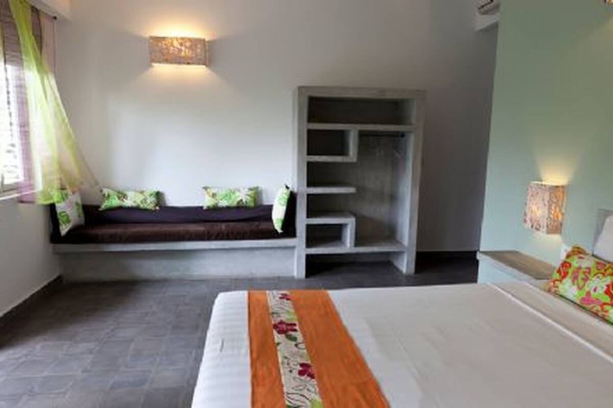 Ein Schlafzimmer mit einem Bett, einer Sitzbank mit Kissen, einem Kleiderschrank und einer Wandleuchte.