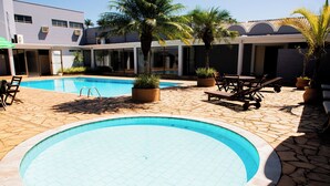 Una piscina con sillones de descanso y plantas en macetas, rodeada por un patio de piedra y un edificio con grandes ventanales.