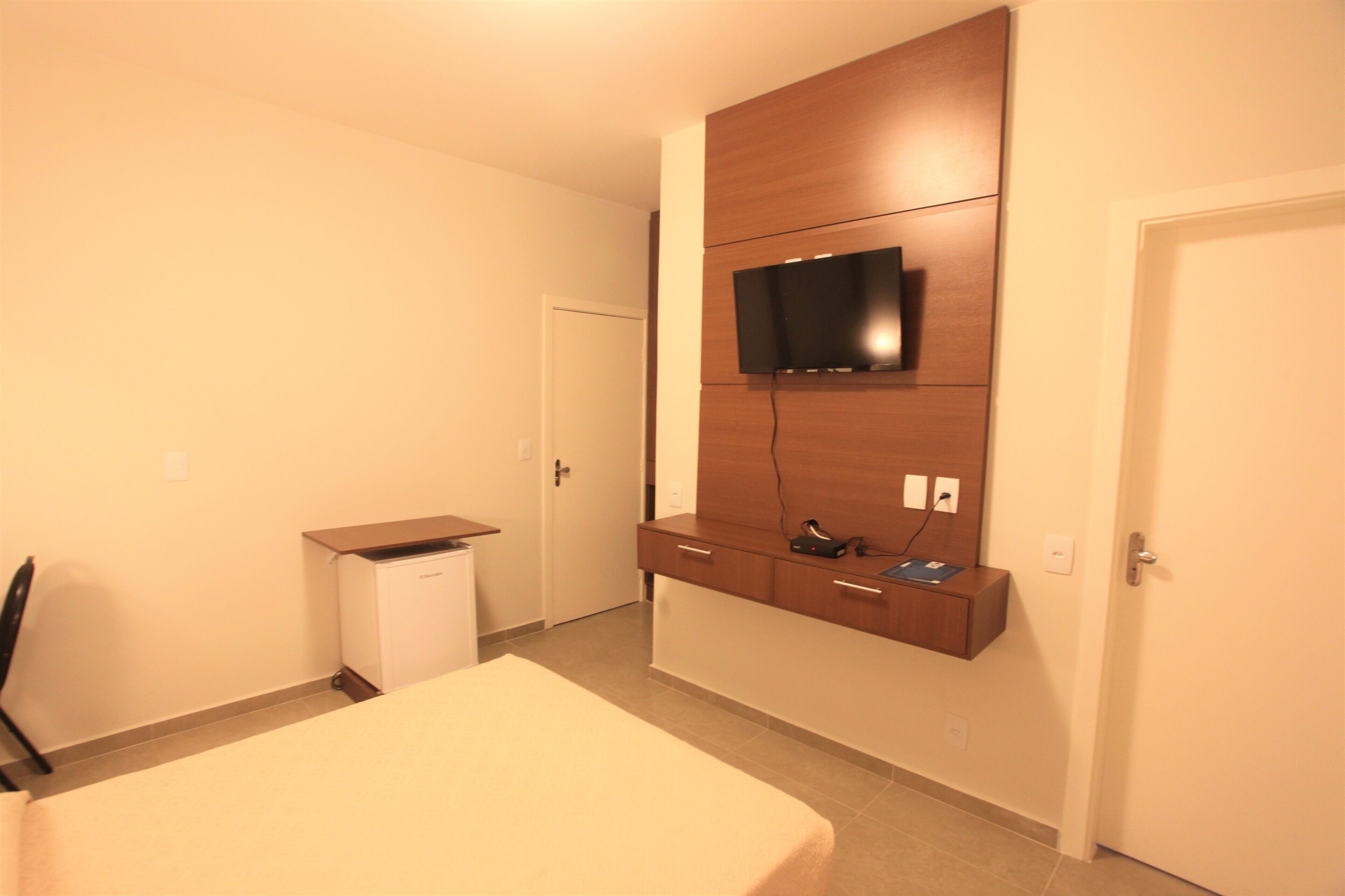 A hotel room with a bed, a desk, a television mounted on the wall, and a door.