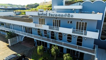 Un hotel con un cartel con su nombre, varios balcones y un estacionamiento.