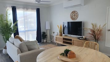 Un salon moderne avec un canapé, un téléviseur, une table basse en bois et des plantes décoratives.