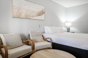 A hotel room with a large bed, two wicker chairs, a round table, and a wall-mounted lamp.