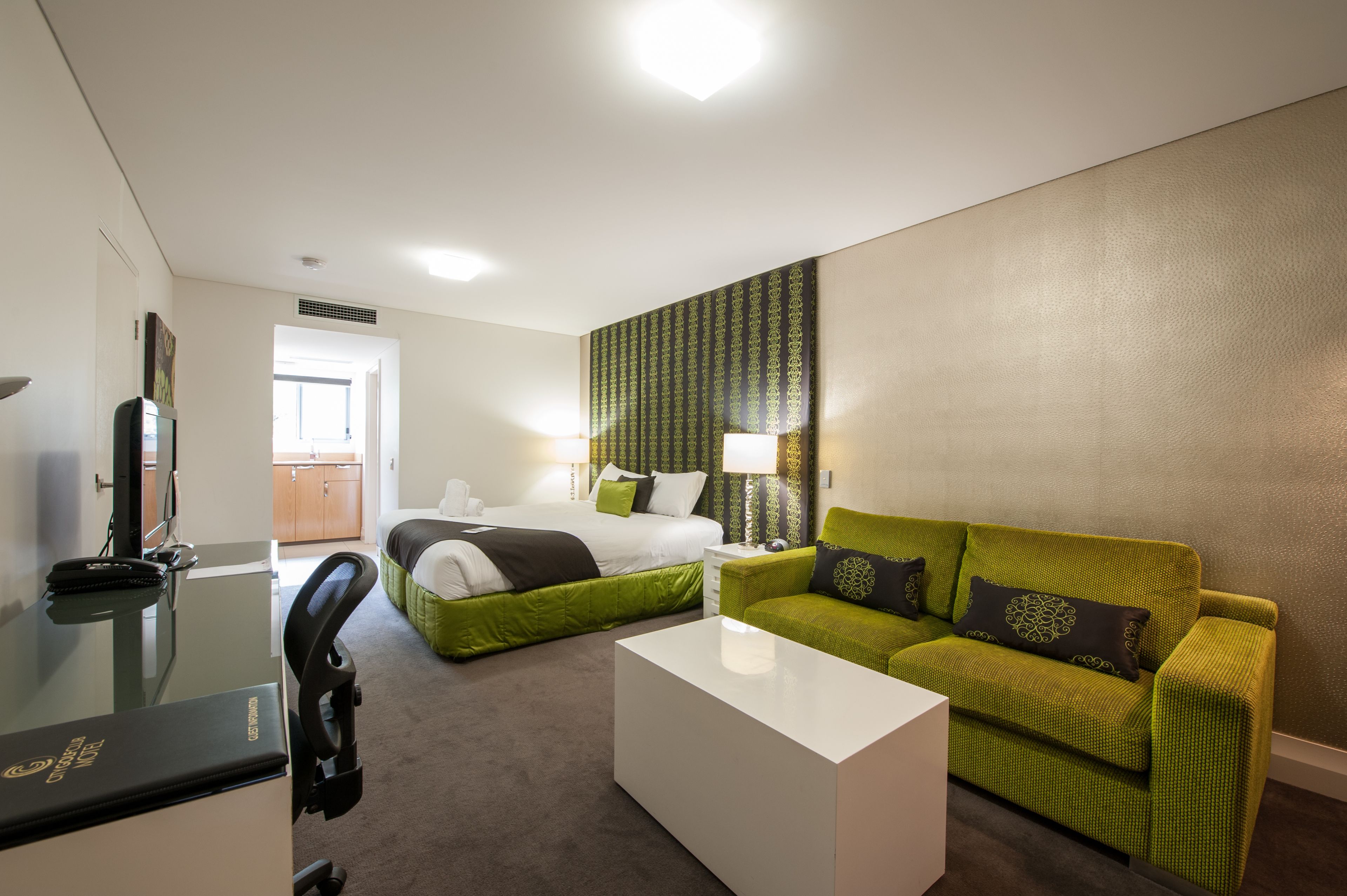 Une chambre d’hôtel avec un lit, un canapé vert, une table basse blanche et un bureau avec un ordinateur.