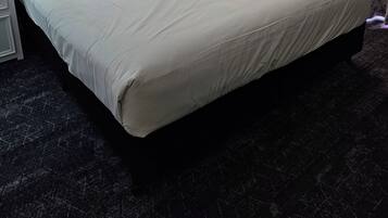 A hotel room with a large bed, a nightstand, a lamp, a window with curtains, and an air conditioning unit.