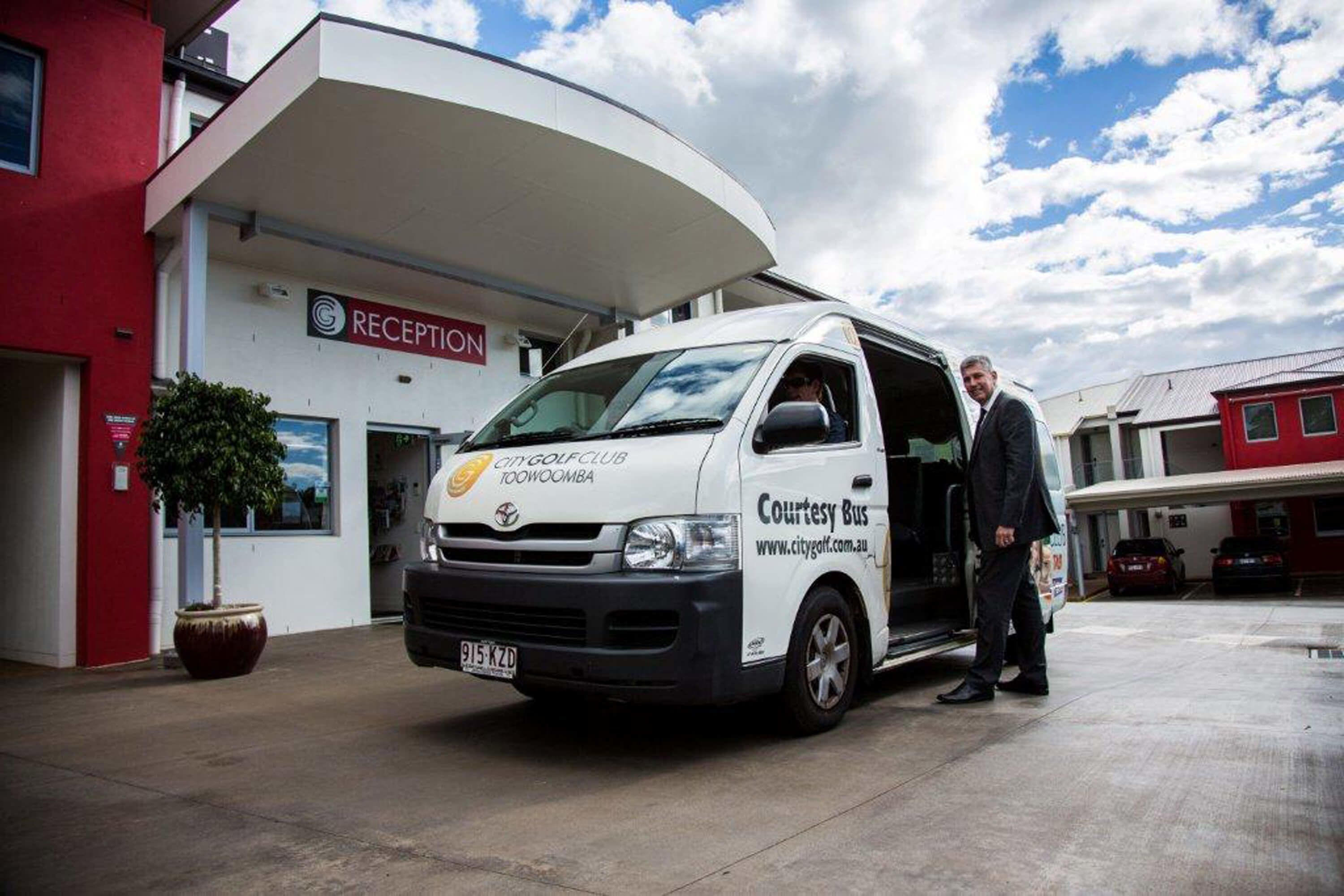 A white van with "Courtesy Bus" and "City Golf Club" branding parked in front of a building with a "RECEPTION" sign.