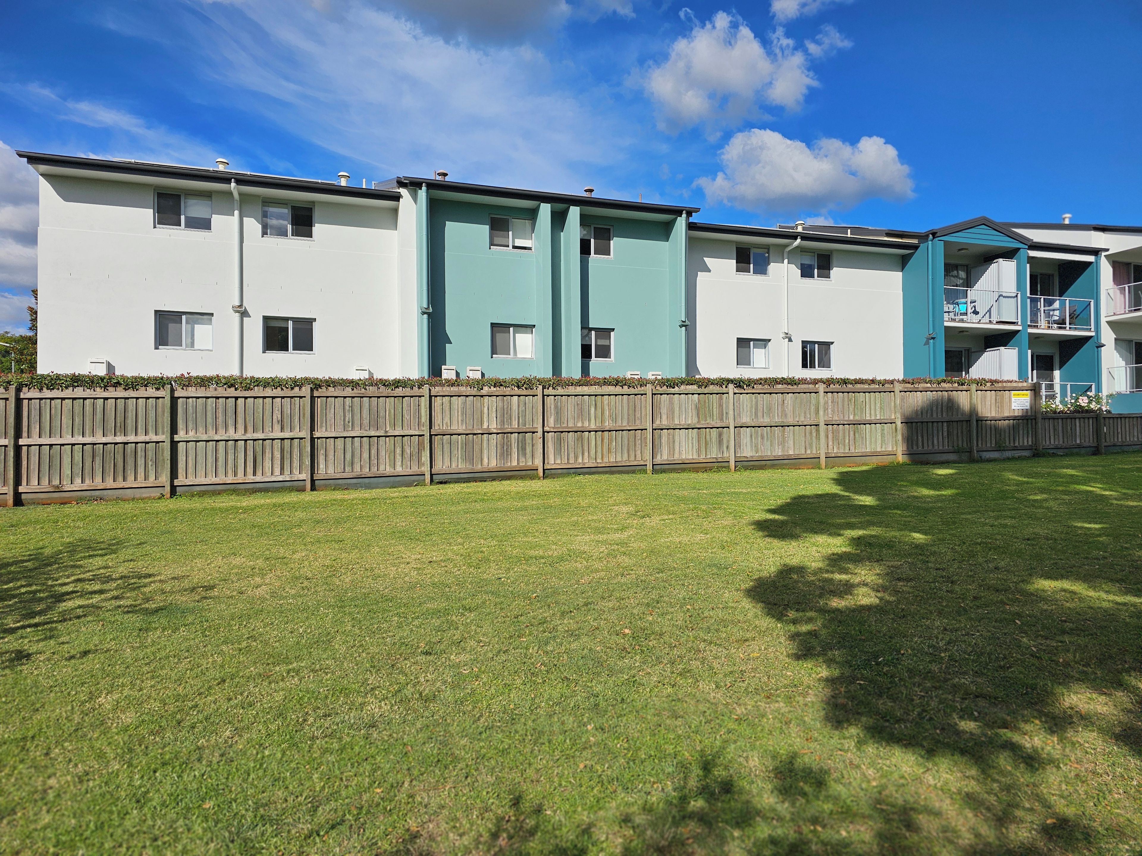 A row of modern multi-story residential buildings with a wooden fence in front.