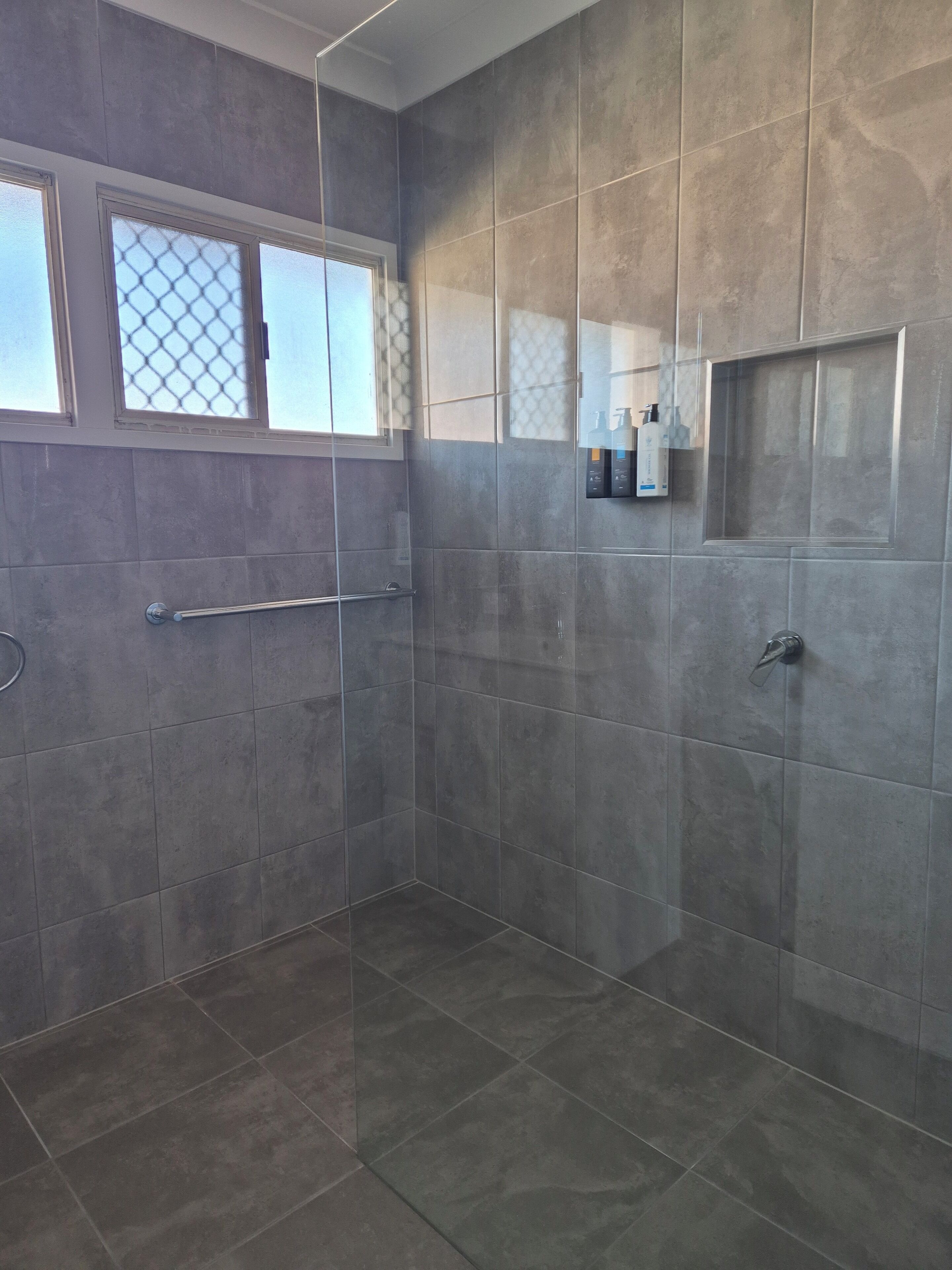 A modern shower area with large tiled walls, a glass door, and a handrail.
