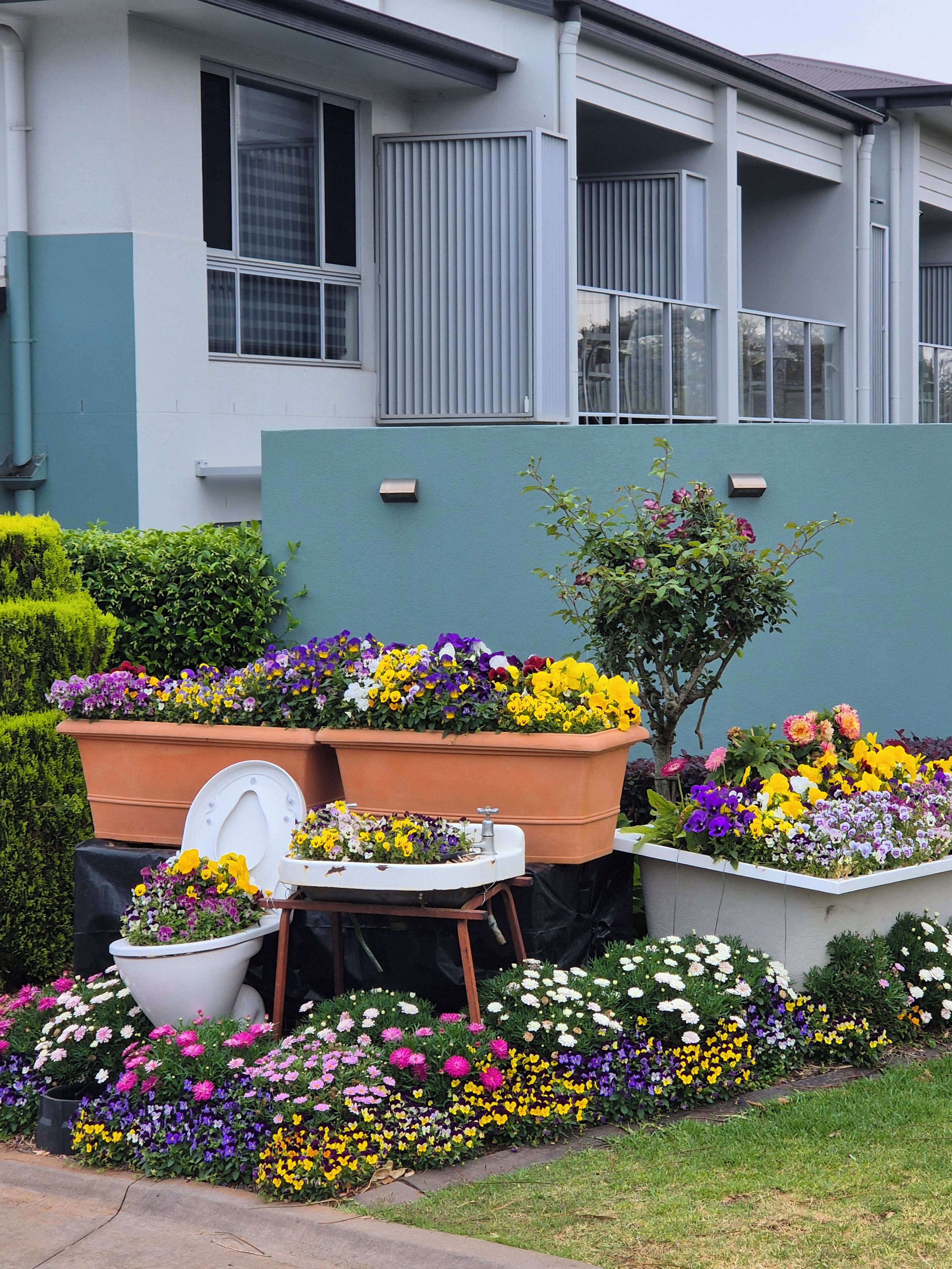Propiedad residencial con jardín delantero que incluye parterres y un baño exterior blanco.