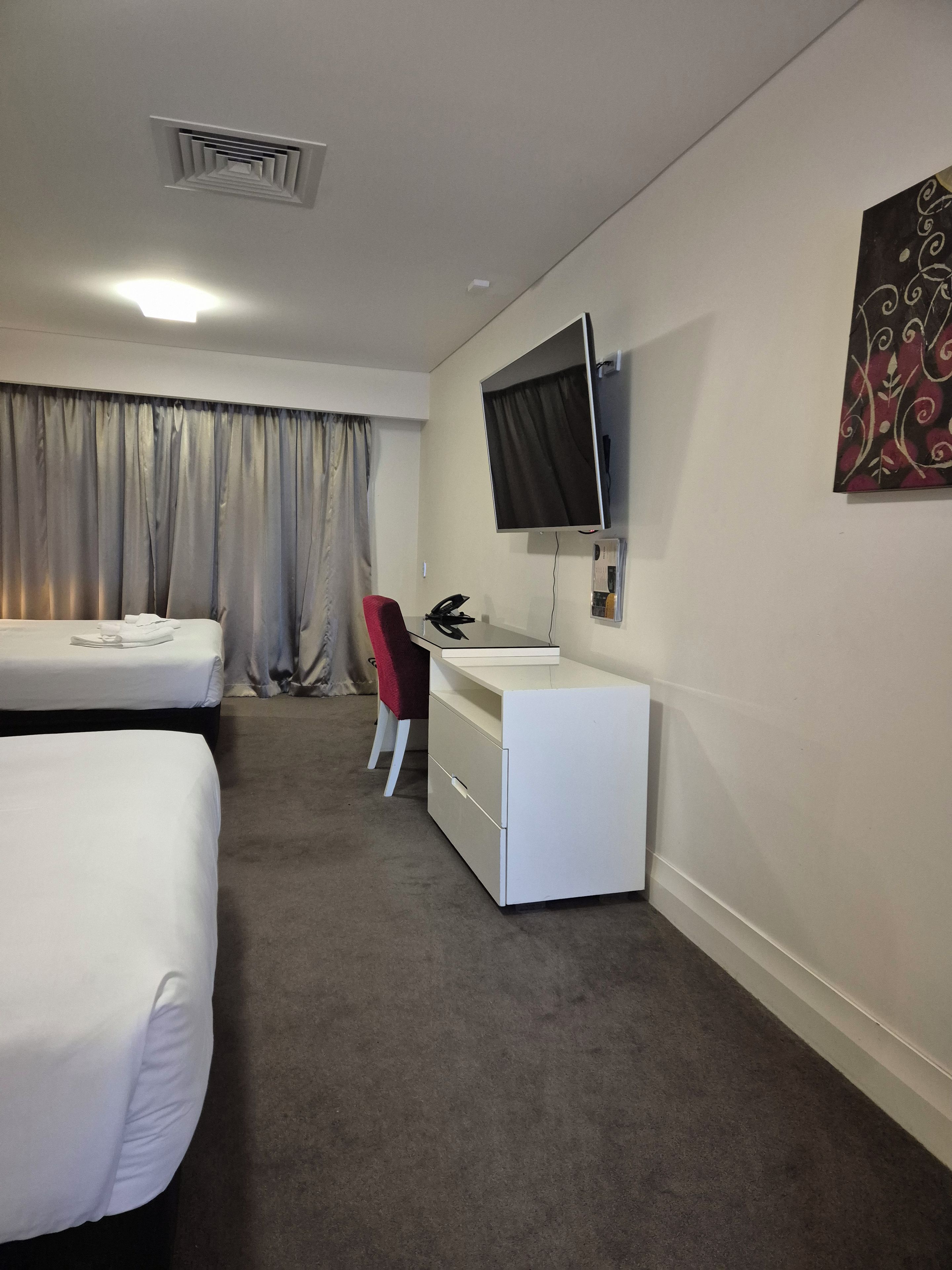Habitación de hotel con dos camas, un escritorio, una silla, un televisor y un cuadro en la pared.