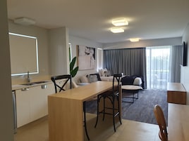 A modern living room with a dining area, a kitchen, and a large window with curtains.