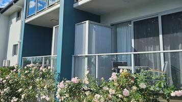 A modern two-story residential building with balconies, large windows, and a garden with flowering plants.