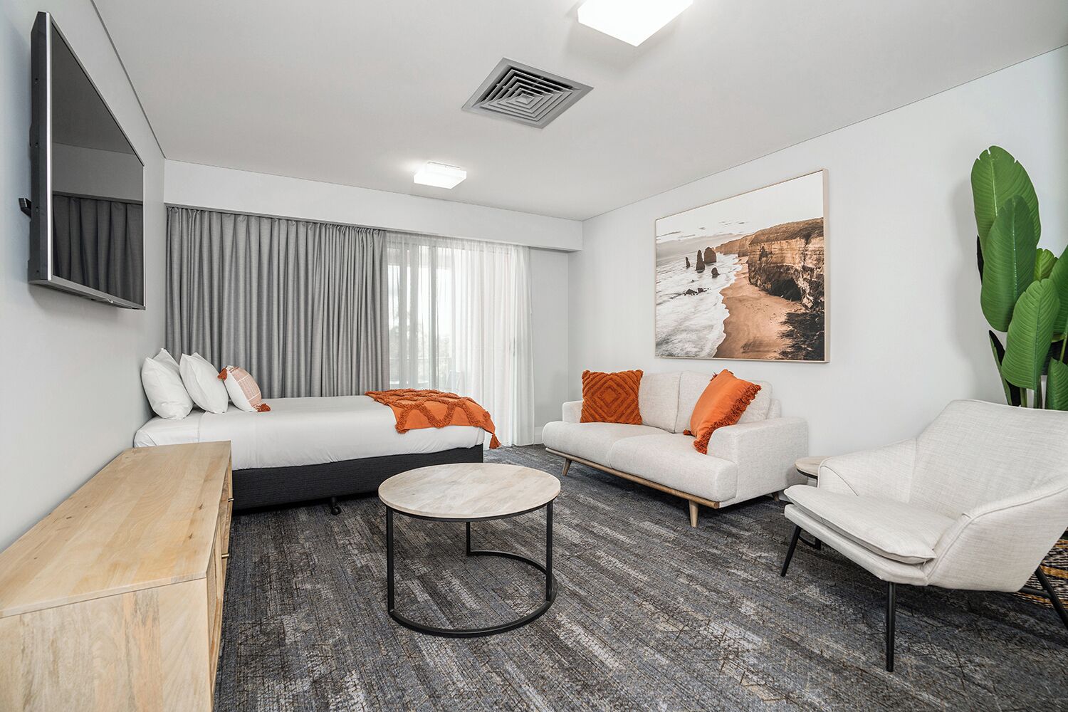 Una habitación de hotel moderna con cama, sofá, sillón y una pequeña mesa redonda.