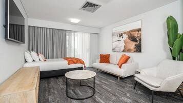 Una habitación de hotel moderna con cama, sofá, sillón y una pequeña mesa redonda.