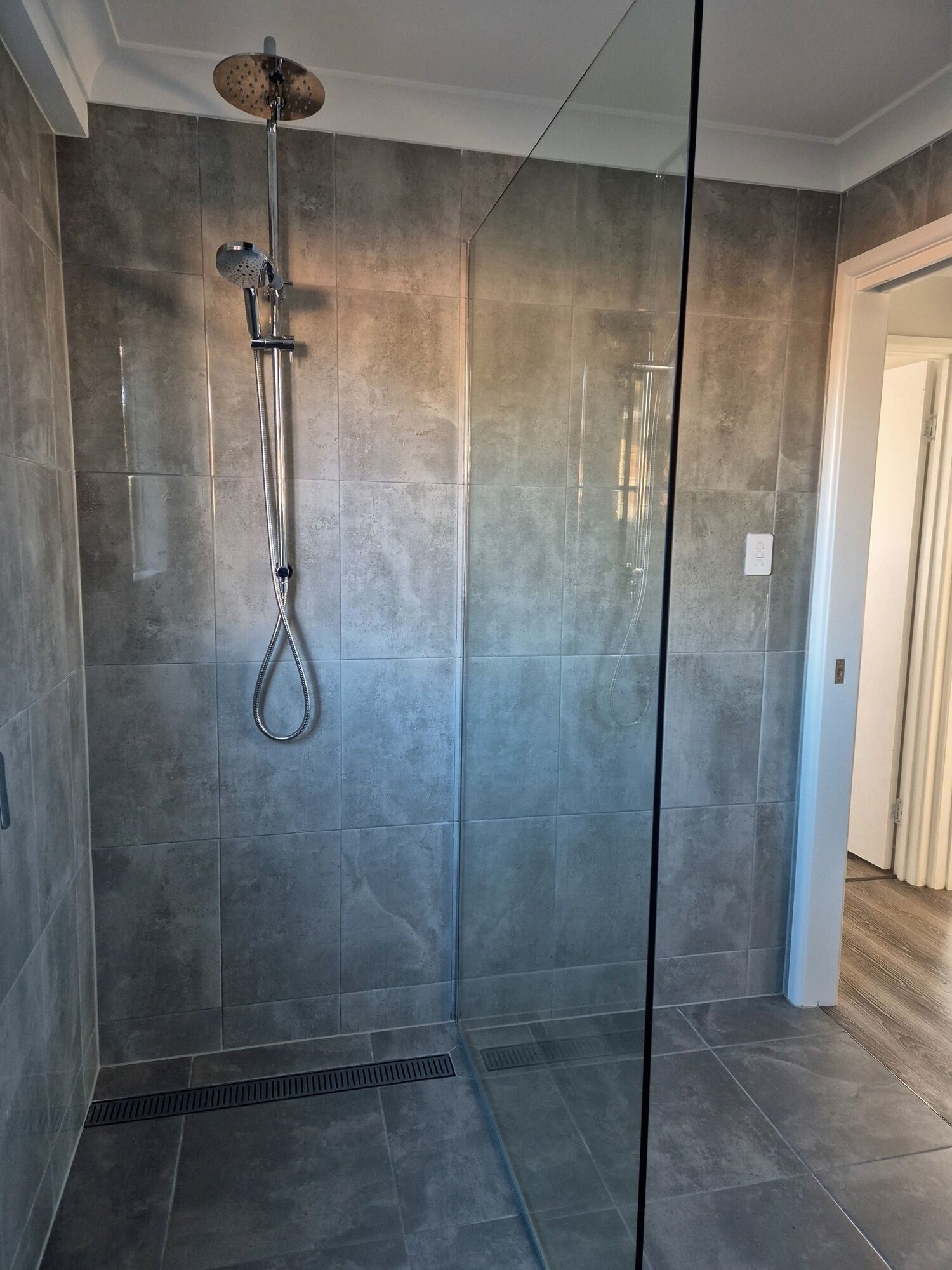 A modern shower with a glass door, grey tiles, and a visible control panel.